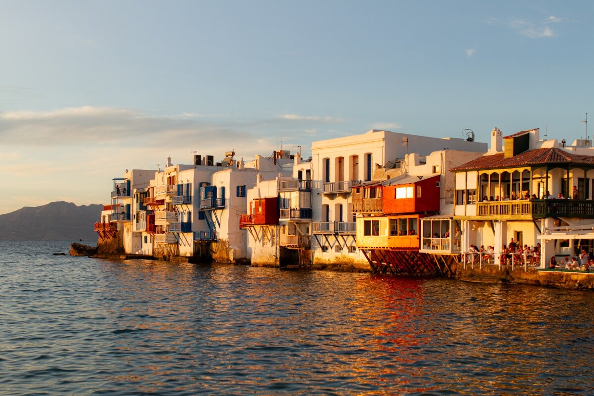 Sunset view of colorful buildings on the waterfront in Little Venice, Mykonos, Greece, with the Aegean Sea reflecting golden sunlight. Ideal for Mykonos wedding packages.