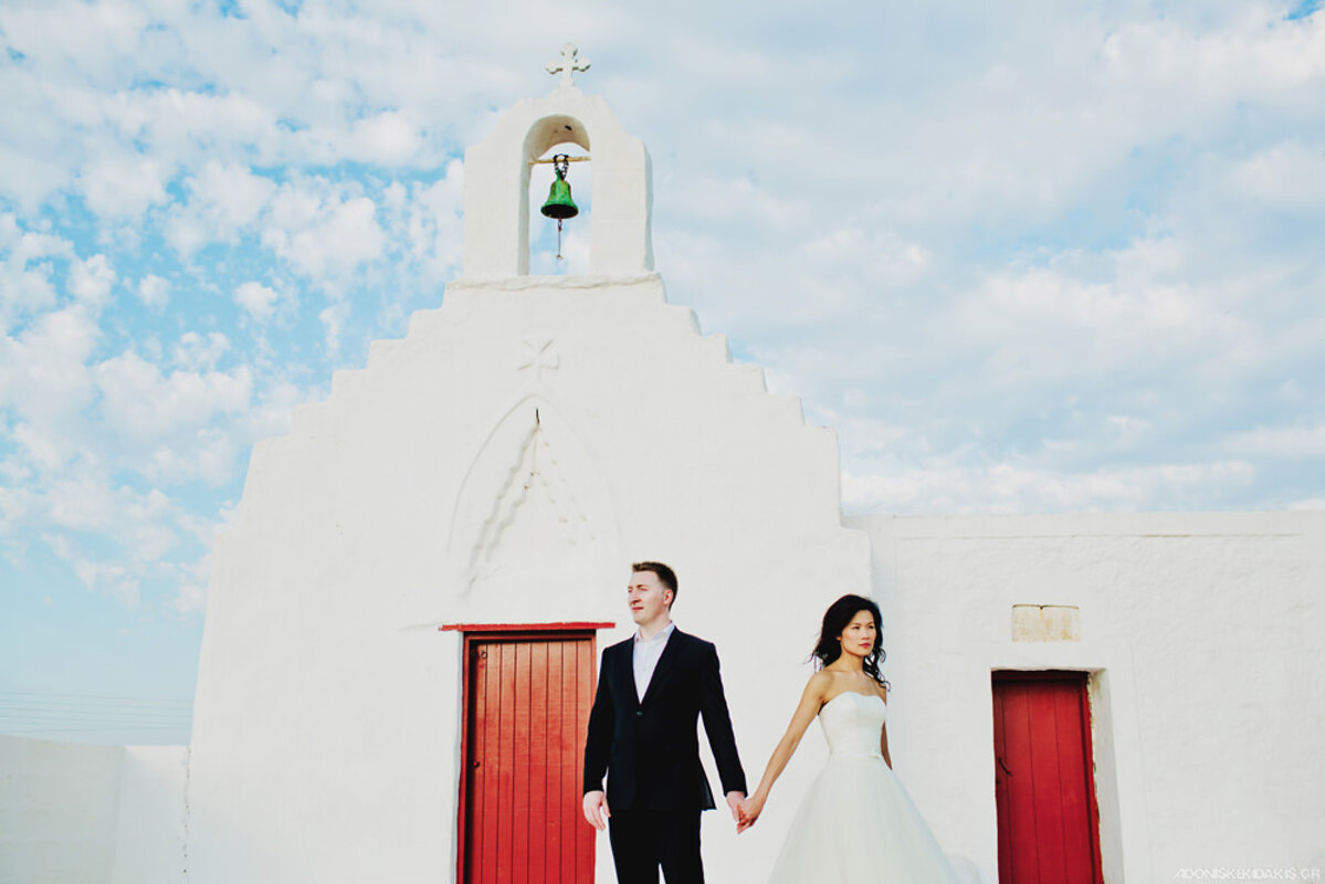 Newly wed couple posing in front of a traditional Orthodox chapels in Mykonos. Mykonos Orthodox wedding packages