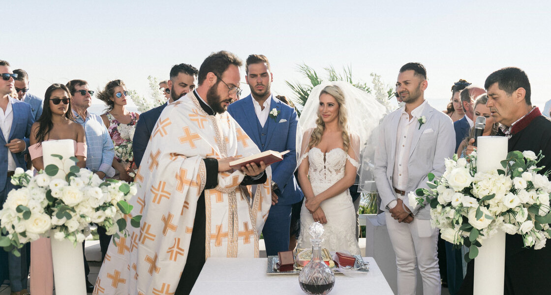 A couple having their Ortodox wedding ceremony by a priest in Mykonos amidst stunning scenery 