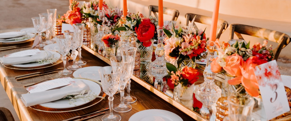 A beautifully arranged wedding reception table in Mykonos, adorned with vibrant red and orange floral decorations.