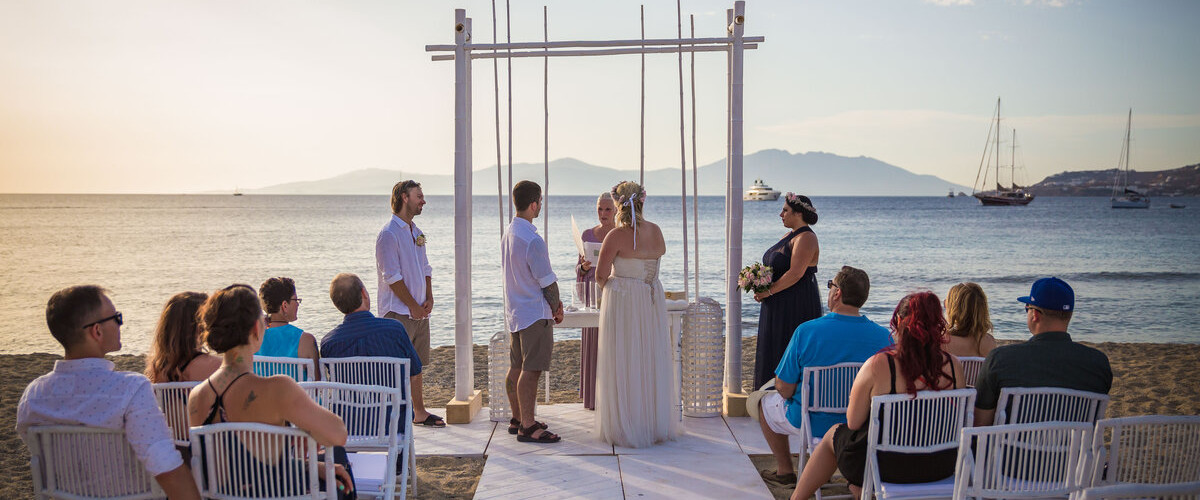 A picturesque Mykonos beach wedding ceremony at sunset, featuring a beautiful backdrop of the sea and sky.