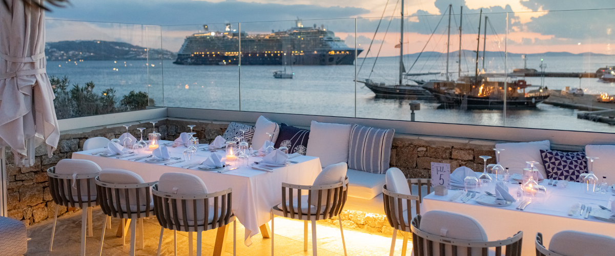 A luxurious Mykonos wedding venue featuring a restaurant with tables and chairs overlooking serene waters.