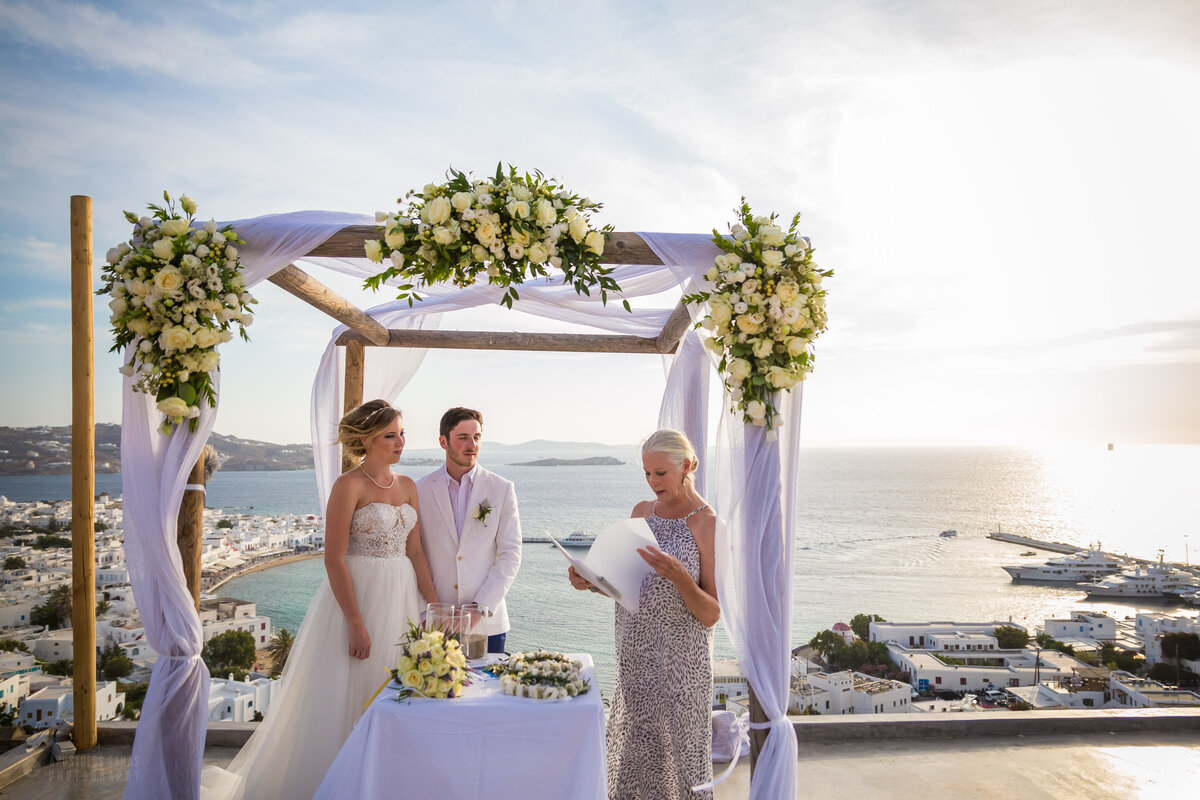 A couple enjoying the words of a wedding celebrant at a beautiful symbolic wedding ceremony set up in Mykonos, showcasing stunning scenery and joyful moments.